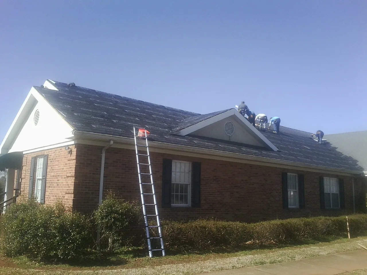 Crew tearing shingles off a brick ranch roof with a ladder set — Emergency Roof Repair work by our crew in Mascoutah