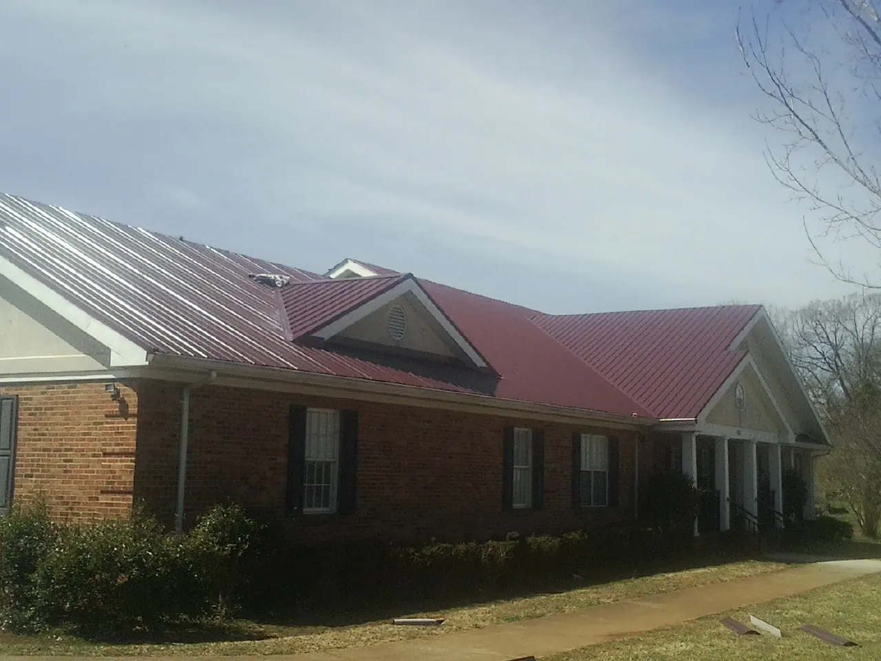 Red metal roof with gabled entries on a long brick building, from a Hail Damage Roof Repair job in Mascoutah