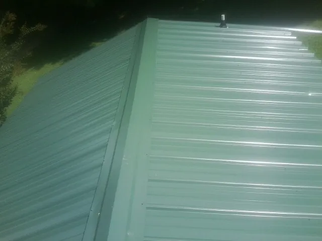 New green metal panels meeting at the ridge of a roof — Flat Roof Repair work by our crew in Mascoutah