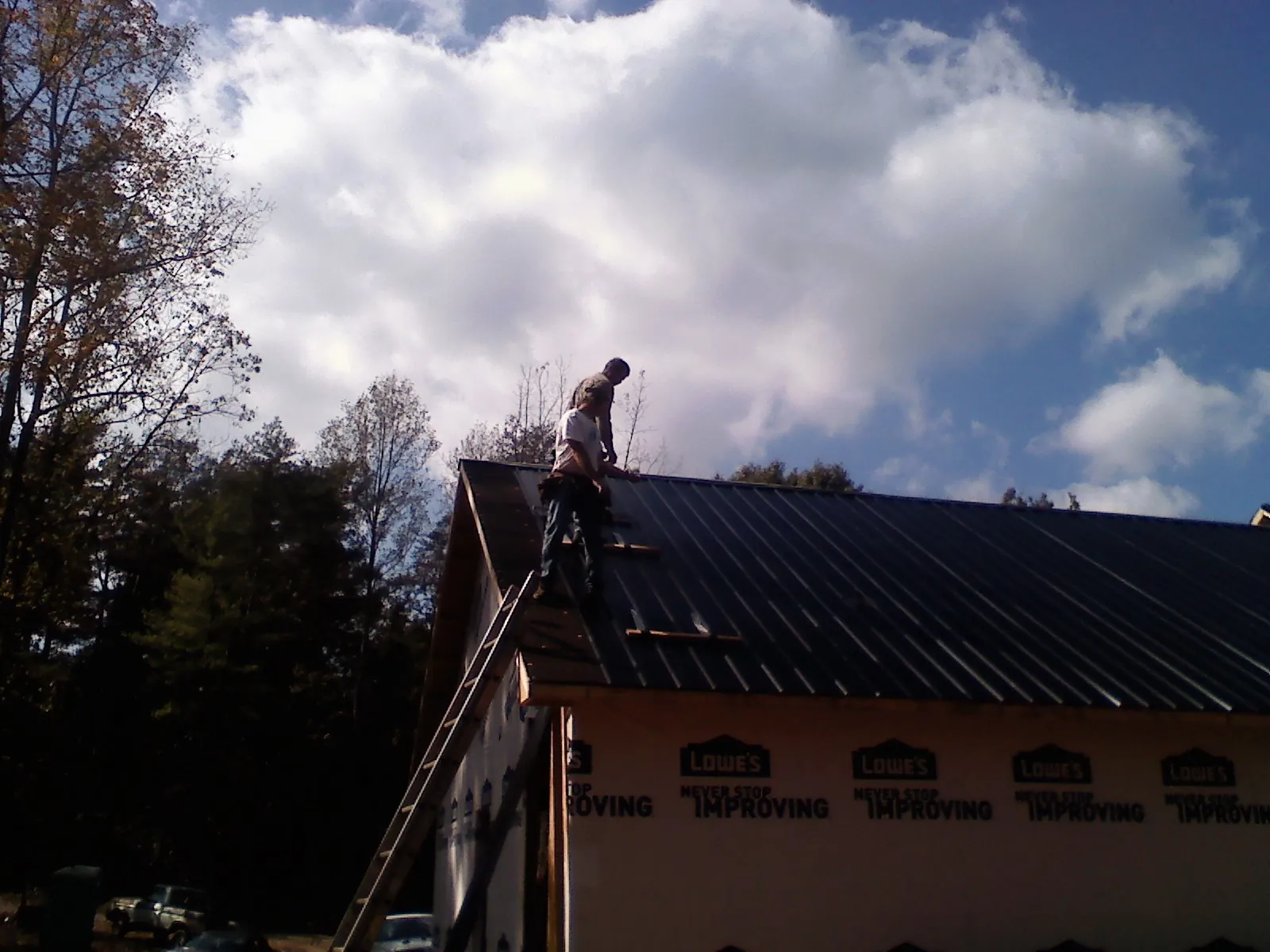 Roofer fastening dark metal panels high against a cloudy sky, from a Roof Inspection job in Mascoutah