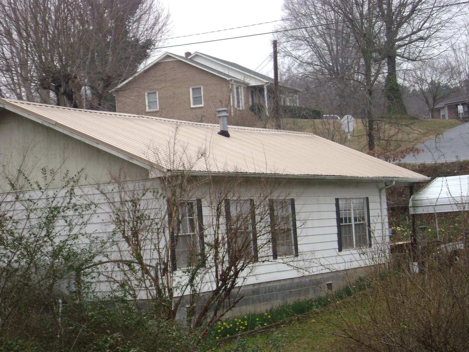Tan metal roof on a white sided house set into a hillside — Commercial Roofing by Roofing Brothers in Mascoutah
